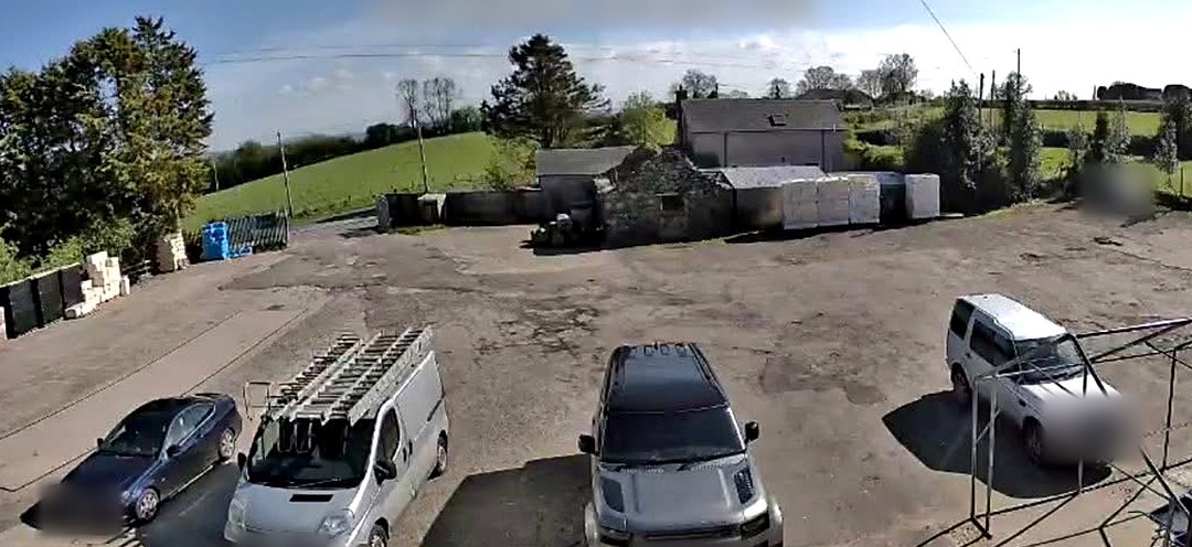 CCTV camera view of a yard with a van and cars parked, number plates blurred